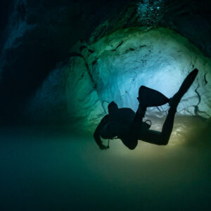 Diver silhouette against a lit limestone alcove in green water, Quintana Roo, Mexico