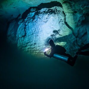 Sidemount diver lighting a pale limestone wall above the haze, Quintana Roo, Mexico