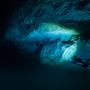 Small diver lighting a blue limestone overhang in a vast cavern, Quintana Roo, Mexico