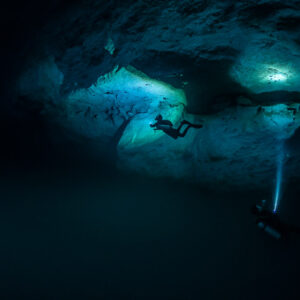 Two divers lighting rock alcoves, one beaming upward from below, Quintana Roo, Mexico