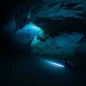 Two divers in a dark cavern, one beaming horizontally, vertical frame, Quintana Roo, Mexico