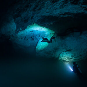 Two divers lighting a green-lit alcove and the wall below, Quintana Roo, Mexico