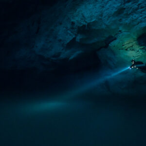 Lone diver beaming torch across a dark cavern beneath an overhang, Quintana Roo, Mexico