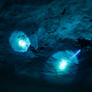 Two divers projecting circles of blue light on a cavern wall, Quintana Roo, Mexico