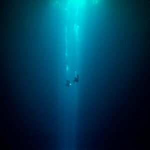 Tiny divers in a vertical shaft of light descending into a dark cenote, Cenote El Zapote, Quintana Roo, Mexico