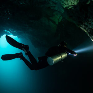 Sidemount diver silhouette lighting a rock edge against blue light, Quintana Roo, Mexico