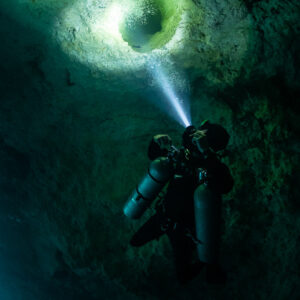 Diver lighting a round hole in the ceiling with his exhaled bubbles, Quintana Roo, Mexico