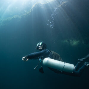 Sidemount diver gliding under sunbeams near the cenote surface, Quintana Roo, Mexico