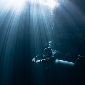 Sidemount diver bathed in sun rays streaming through the water, Quintana Roo, Mexico