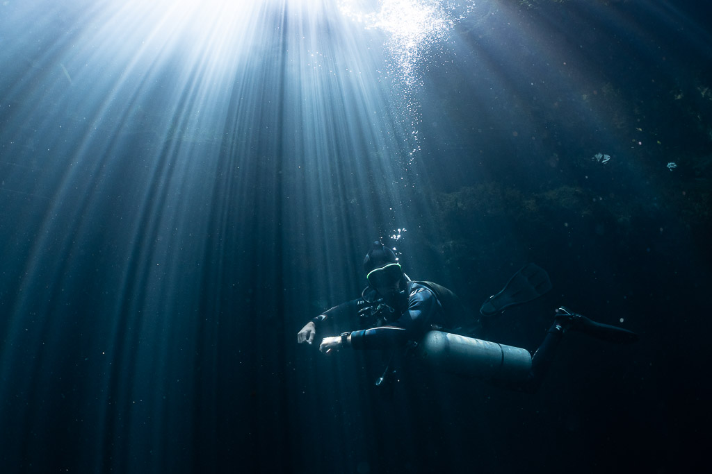 Plongeur en sidemount baigné de rayons de soleil traversant l’eau, Quintana Roo, Mexique