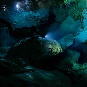 Sidemount diver lighting a passage in shallow cavern with surface reflections, Quintana Roo, Mexico