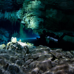 Sidemount diver lighting a fringe of stalactites over a rocky floor, Quintana Roo, Mexico