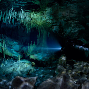 Diver beaming torch beneath dense stalactites and surface reflections, Quintana Roo, Mexico