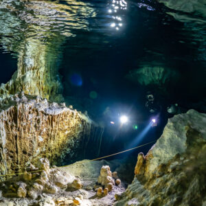 Divers with torches behind golden flowstone draperies near the surface, Quintana Roo, Mexico