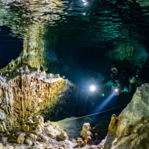 Divers lighting a cavern of golden flowstone curtains and pillars, Quintana Roo, Mexico