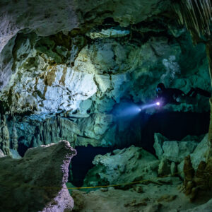 Diver lighting a white limestone chamber with slender columns, Quintana Roo, Mexico