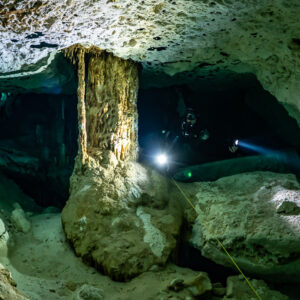 Diver lighting the passage behind a thick limestone column, Quintana Roo, Mexico