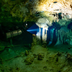 Sidemount diver lighting a pale column in a green cavern, Quintana Roo, Mexico