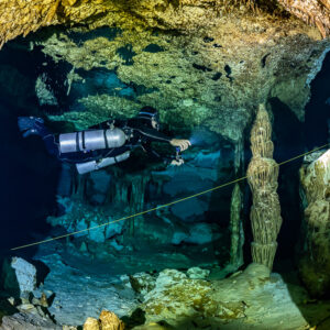Sidemount diver framed between two golden columns along a guideline, Quintana Roo, Mexico