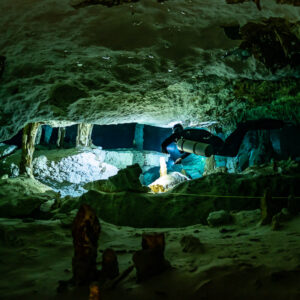 Sidemount diver crossing a low chamber with a guideline and stalagmites, Quintana Roo, Mexico
