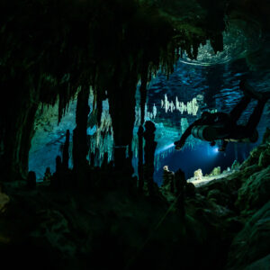 Diver silhouette behind dark stalactites against a bright opening, Quintana Roo, Mexico
