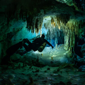 Diver silhouette lighting the floor under hanging stalactites, Quintana Roo, Mexico