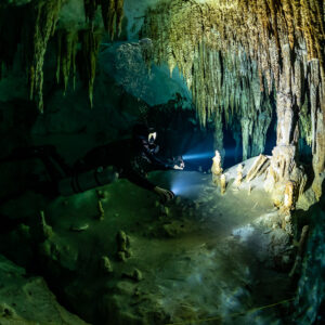 Sidemount diver lighting a stalagmite under a stalactite curtain, Quintana Roo, Mexico