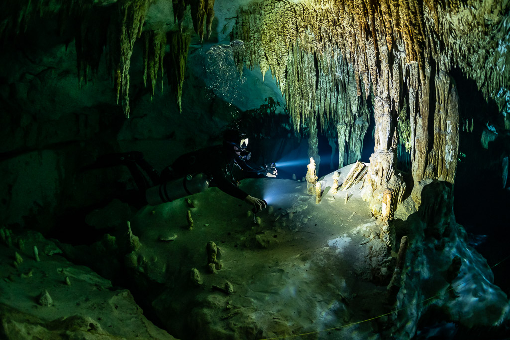 Plongeur en sidemount éclairant une stalagmite sous un rideau de stalactites, Quintana Roo, Mexique