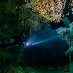 Sidemount diver beaming torch beside a guideline under a decorated ceiling, Quintana Roo, Mexico