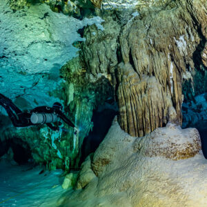 Sidemount diver next to a large flowstone formation in blue water, Quintana Roo, Mexico
