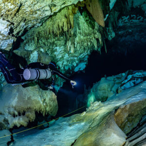 Sidemount diver close-up passing pale rocks with torch on, Quintana Roo, Mexico