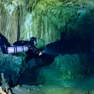 Sidemount diver lighting a dark tunnel beneath stalactites, Quintana Roo, Mexico