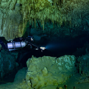 Sidemount diver beaming into a tunnel past a lone stalagmite, Quintana Roo, Mexico