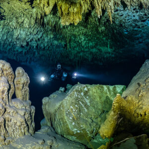 Divers with torches behind a cluster of stalagmites and a large block, Quintana Roo, Mexico