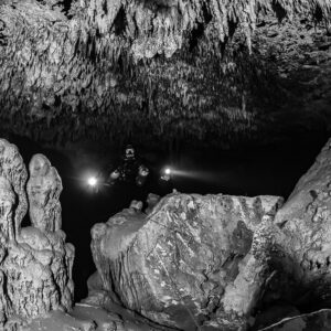 Black and white divers behind a stalagmite cluster and a large block, Quintana Roo, Mexico