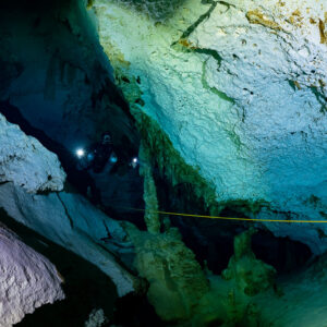 Diver lighting a narrow gap beside a huge pale boulder, Quintana Roo, Mexico