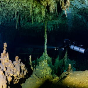 Sidemount diver beyond golden stalagmites under a stalactite ceiling, Quintana Roo, Mexico