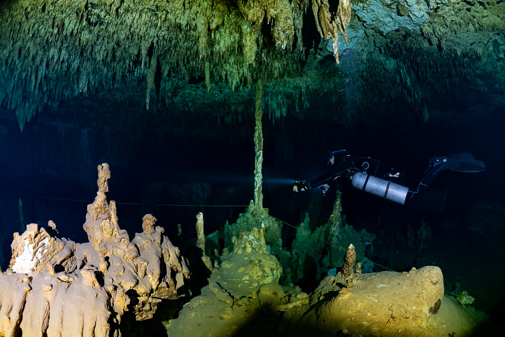 Plongeur en sidemount derrière des stalagmites dorées sous un plafond de stalactites, Quintana Roo, Mexique