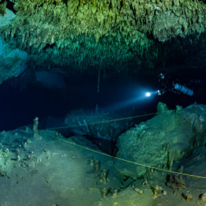 Sidemount diver beaming into a dark passage beside a guideline, Quintana Roo, Mexico
