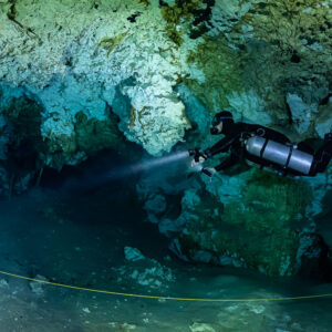 Sidemount diver lighting a blue passage with a guideline below, Quintana Roo, Mexico