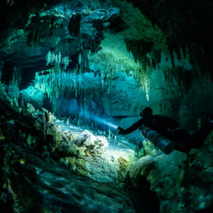 Sidemount diver lighting a tunnel framed by stalactites, Quintana Roo, Mexico