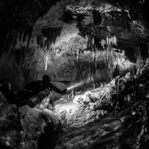 Black and white diver lighting a tunnel framed by stalactites, Quintana Roo, Mexico