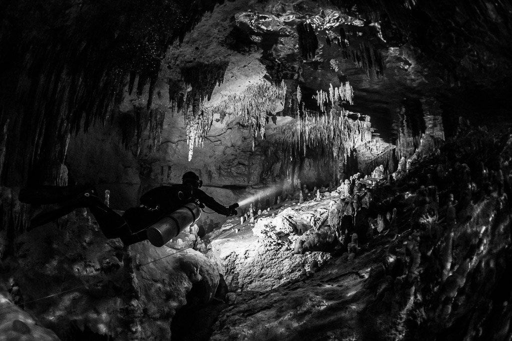 Plongeur éclairant un tunnel encadré de stalactites, noir et blanc, Quintana Roo, Mexique