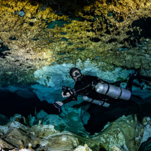 Sidemount diver with camera among cave formations below the ceiling, Quintana Roo, Mexico