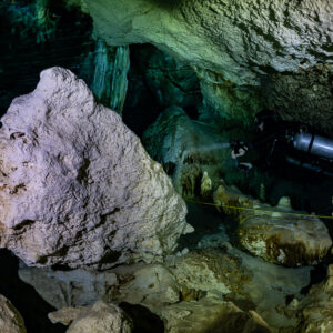 Sidemount diver lighting a passage past a large pale boulder, Quintana Roo, Mexico