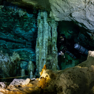 Sidemount diver between pillars behind a golden lit rock, Quintana Roo, Mexico