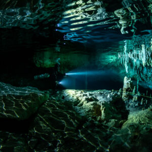 Diver beaming torch under rippled surface reflections and stalactites, Quintana Roo, Mexico