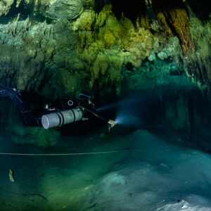Sidemount diver gliding over a pale slope beside a guideline, Quintana Roo, Mexico