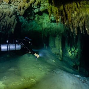 Sidemount diver touching down on a sandy slope under stalactites, Quintana Roo, Mexico