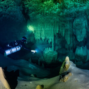 Sidemount diver lighting stalagmites below a green stalactite curtain, Quintana Roo, Mexico